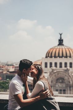 a man and woman kissing on the roof of a building with a dome in the background