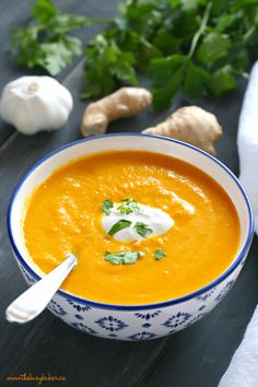 a bowl of carrot soup with sour cream and parsley on the table next to it