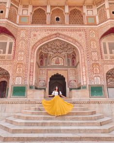 a woman in white shirt and yellow skirt standing on steps with stairs leading up to an ornate building