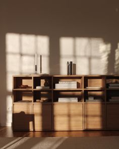 a book shelf with books and candles on it in front of a window that has sunlight streaming through the windows