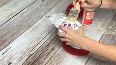 a woman is using a brush to paint the top of a doily on a wooden table