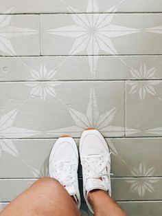 a person's legs and white sneakers on a tiled floor