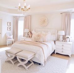 a white bedroom with a chandelier hanging from the ceiling and a large bed