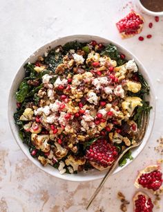 a white bowl filled with food and topped with pomegranates next to a cup of coffee