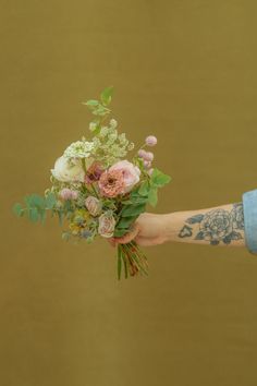 a person holding a bouquet of flowers in their hand with tattoos on the arm and wrist