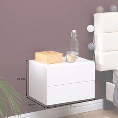 a white nightstand with a bottle on it next to a plant and bedding in a room