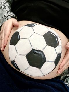 a pregnant woman holding a soccer ball painted on her belly