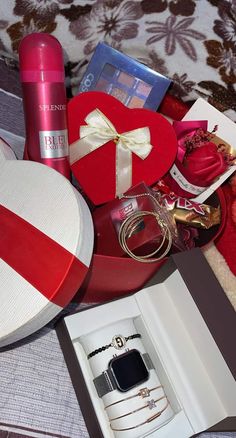 an open gift box on a bed with jewelry and other items in the box next to it