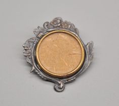 a small silver and gold brooch with an oval design on the front, sitting on a gray surface