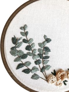 a close up of a embroidery on a white cloth with flowers and leaves in it