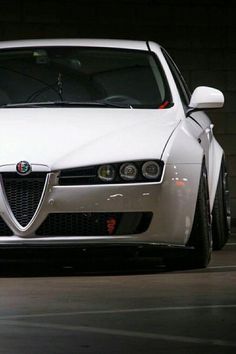 a white car parked in front of a brick wall with its hood up and lights on