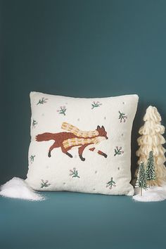 a decorative pillow with a fox on it next to a small pine tree and snow