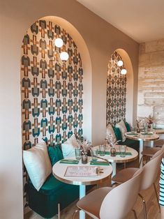 the interior of a restaurant with white tables and green chairs, patterned wall behind them