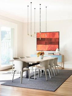 a dining room table with white chairs and a large painting on the wall