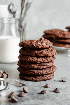 a stack of chocolate cookies next to a glass of milk and spoons on a table