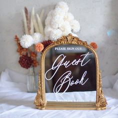 a sign that says guest book on it next to flowers and a vase with white carnations