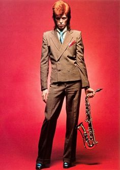 a man in a suit and tie holding a saxophone against a red background with his hands on his hips