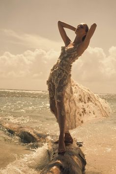 a woman standing in the ocean with her arms behind her head wearing a white dress