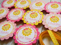 some pink and yellow tags with sun faces on them, sitting next to a ribbon