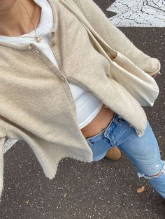 a woman in ripped jeans and a white shirt is standing on the street with her hands behind her back