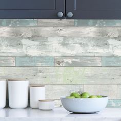 a bowl of green apples sitting on top of a counter next to two white cups