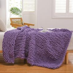 a purple knitted blanket sitting on top of a bed