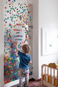 a young boy standing in front of a wall covered with letters and numbers on it