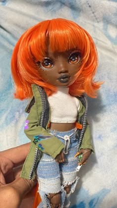 a doll with orange hair is posed on a blue and white background, wearing ripped jeans