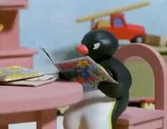 a toy penguin sitting at a table reading a magazine