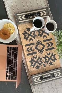 an open laptop computer sitting on top of a wooden table next to two cups of coffee