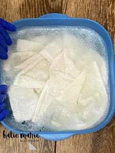 two hands in blue gloves are cleaning a bowl of ice cubes on a wooden table