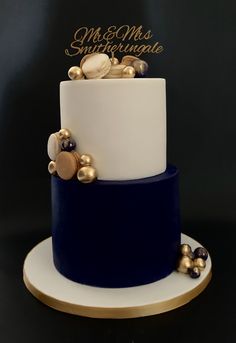 a white and blue wedding cake with gold decorations on the top, sitting on a plate