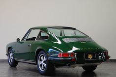 a green porsche is parked in a room with black tile flooring and white walls