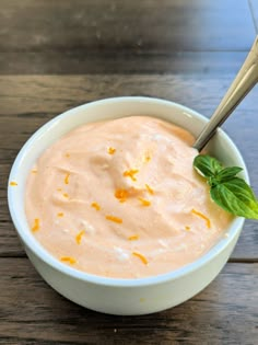 a white bowl filled with orange sauce on top of a wooden table next to a spoon