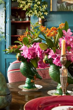 pink flowers are in green vases on the dining room table with candlesticks