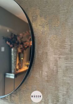 a round mirror hanging on the side of a wall next to a vase with flowers