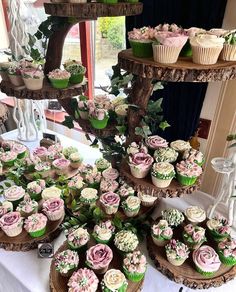 cupcakes are arranged on three tiered trays with greenery and pink flowers