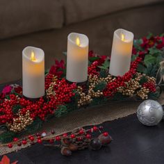 three lit candles are sitting on a table with holly and red berries around the edges