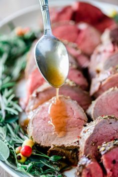 a fork is being used to drizzling sauce on sliced meat with herbs