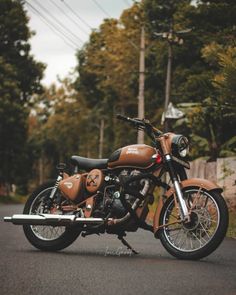 a brown motorcycle parked on the side of a road next to power lines and trees