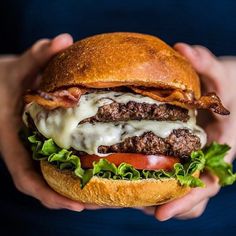 a person holding a large hamburger with cheese and lettuce on it, in their hands