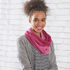 a woman wearing a pink knitted scarf and smiling at the camera with her hands in her pockets