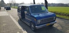 an old blue van parked on the side of a road next to a park area