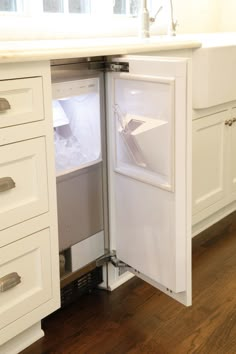 an open refrigerator door in a kitchen with white cabinets and wood flooring on the side