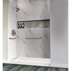 a bathroom with marble tile and white walls, including a walk in shower stall that has shelves on the wall