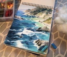 a spiral notebook with an image of the ocean on it next to some crayons