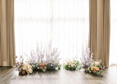 the flowers are arranged on the floor in front of the window with curtains behind them