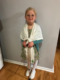 an older woman with glasses and a white scarf is standing on crutches in front of a wall