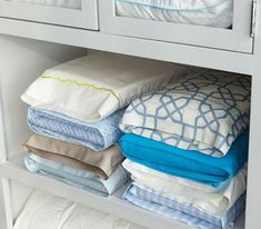 a white shelf filled with lots of folded sheets and pillow cases on top of each other