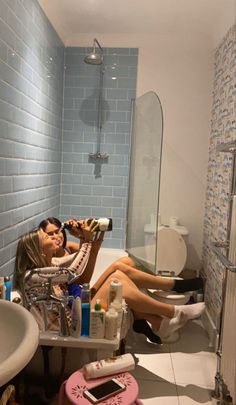 two women sitting in a bathroom with blue tiles